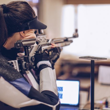 One woman, girl sport shooter aiming with a rifle on target shooting training.